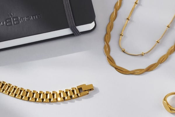 Exquisites Goldschmuck-Display und Marken-Notizbuch von Bijou Brigitte auf weißer Oberfläche.