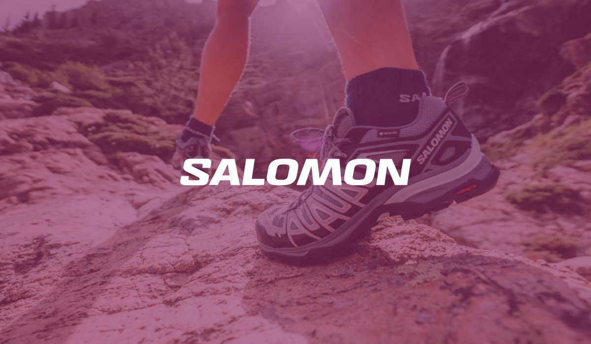 Adventurous hiker exploring mountains with Salomon sneakers, prominently featuring the SALOMON logo in the foreground.