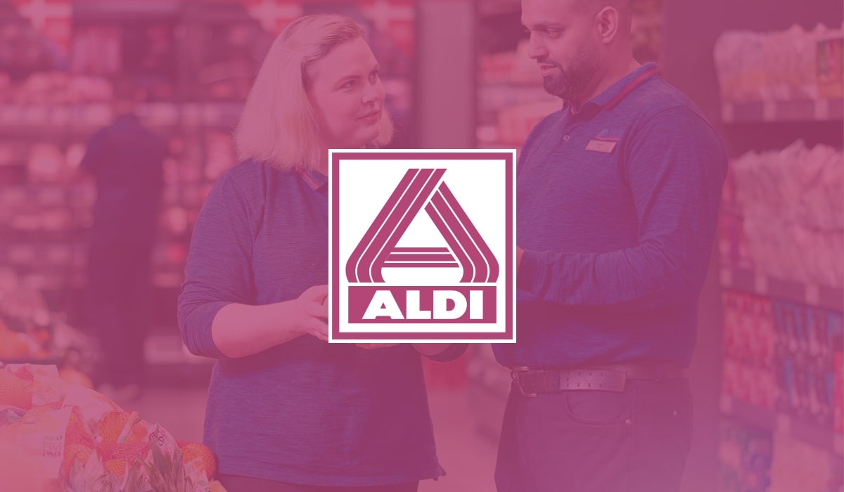 ALDI supermarket employees discussing workforce management solutions in the aisle, with the ALDI logo visible in the foreground. 