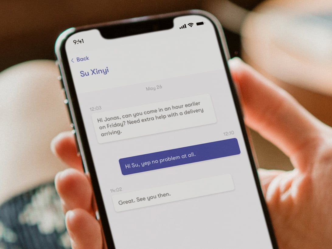 Employee Jonas holding a phone, displaying a chat conversation with his store manager Su discussing an earlier shift start.